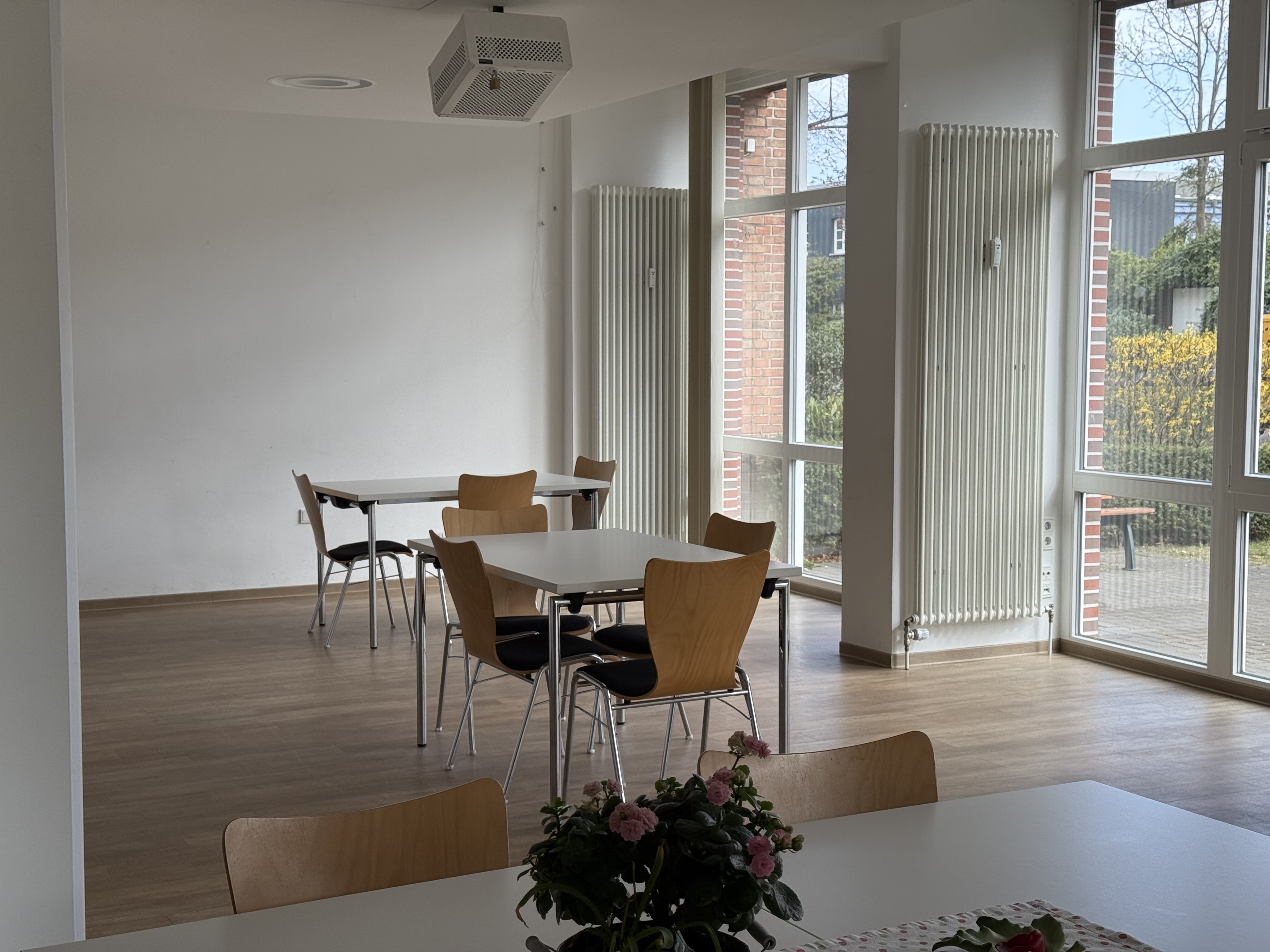 Blick in den Nachbarschaftstreff, Tische mit Stühlen und die Fensterfront sind zu sehen